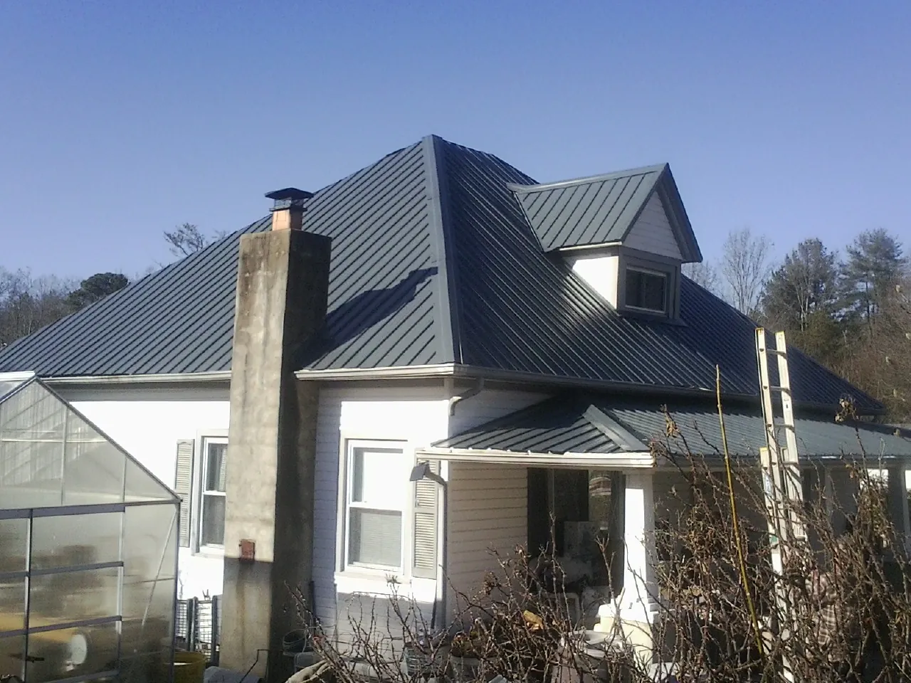 Dark blue standing seam metal roof on a white farmhouse with dormer — Slate & Tile Roof Repair by Roofing Brothers in Dendron