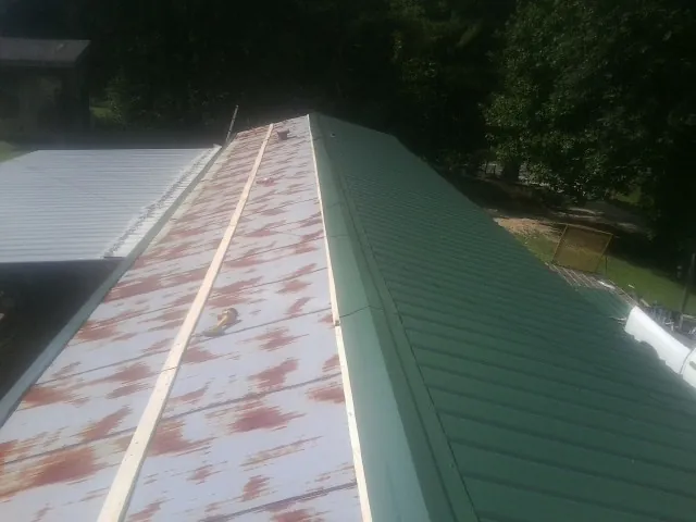 Old rusted panels beside newly installed green metal roofing — Wind Damage Roof Repair by Roofing Brothers in Dendron