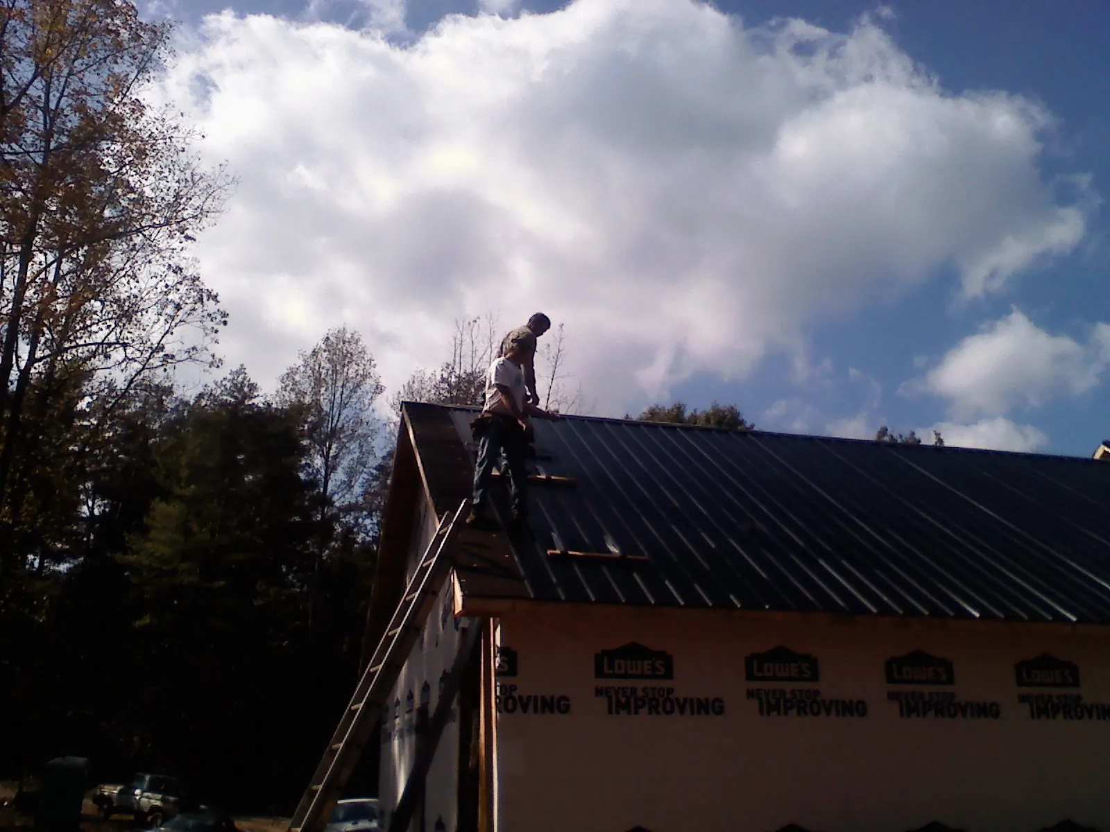 Roofer fastening dark metal panels high against a cloudy sky, from a Roof Inspection job in Dendron